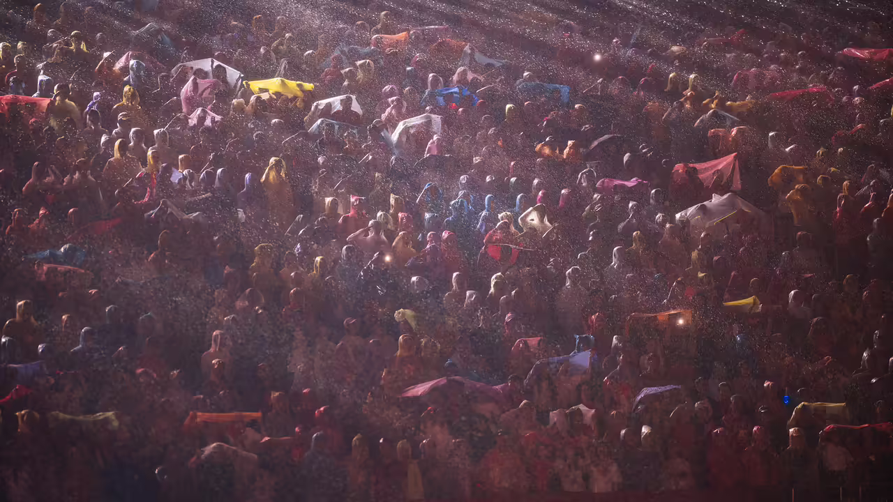 Crowd of people in rain with light cones from reflectors.